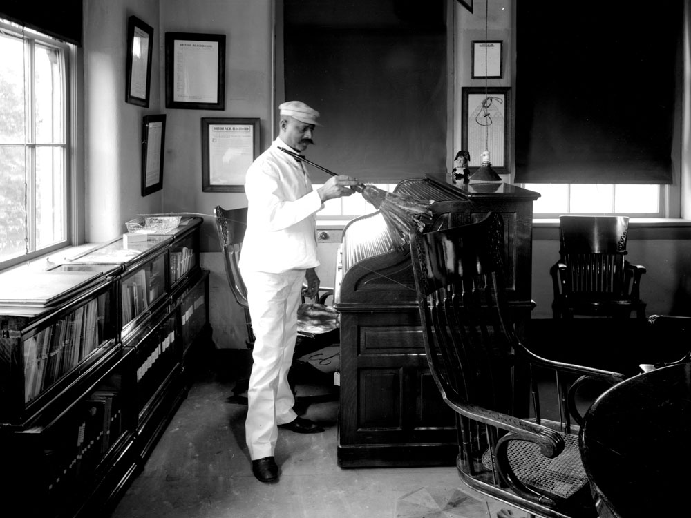 Black janitor dusting John Patterson's office at NCR